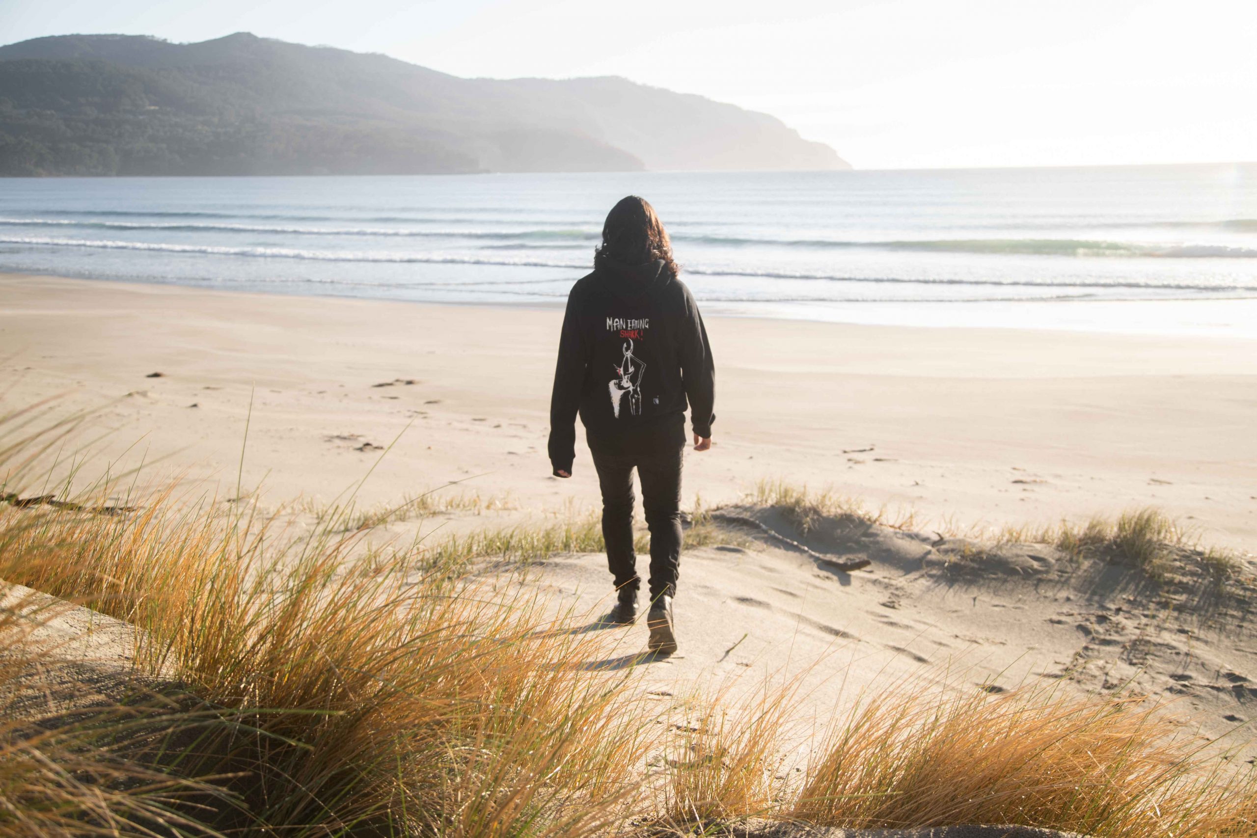 Man walking down to the beach in sunset wearing black Man Eating Shark Hoodie with Punk design Tasmania